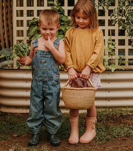 A young boy wearing an overalls next to a young girl holding a garden basket