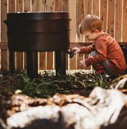 a child playing outside by a large black compost