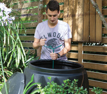a man using a Compost Mate tool to stir and mix organic materials inside a compost bin
