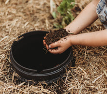 a hand of a young child adding soil inside a worm buffet bucket